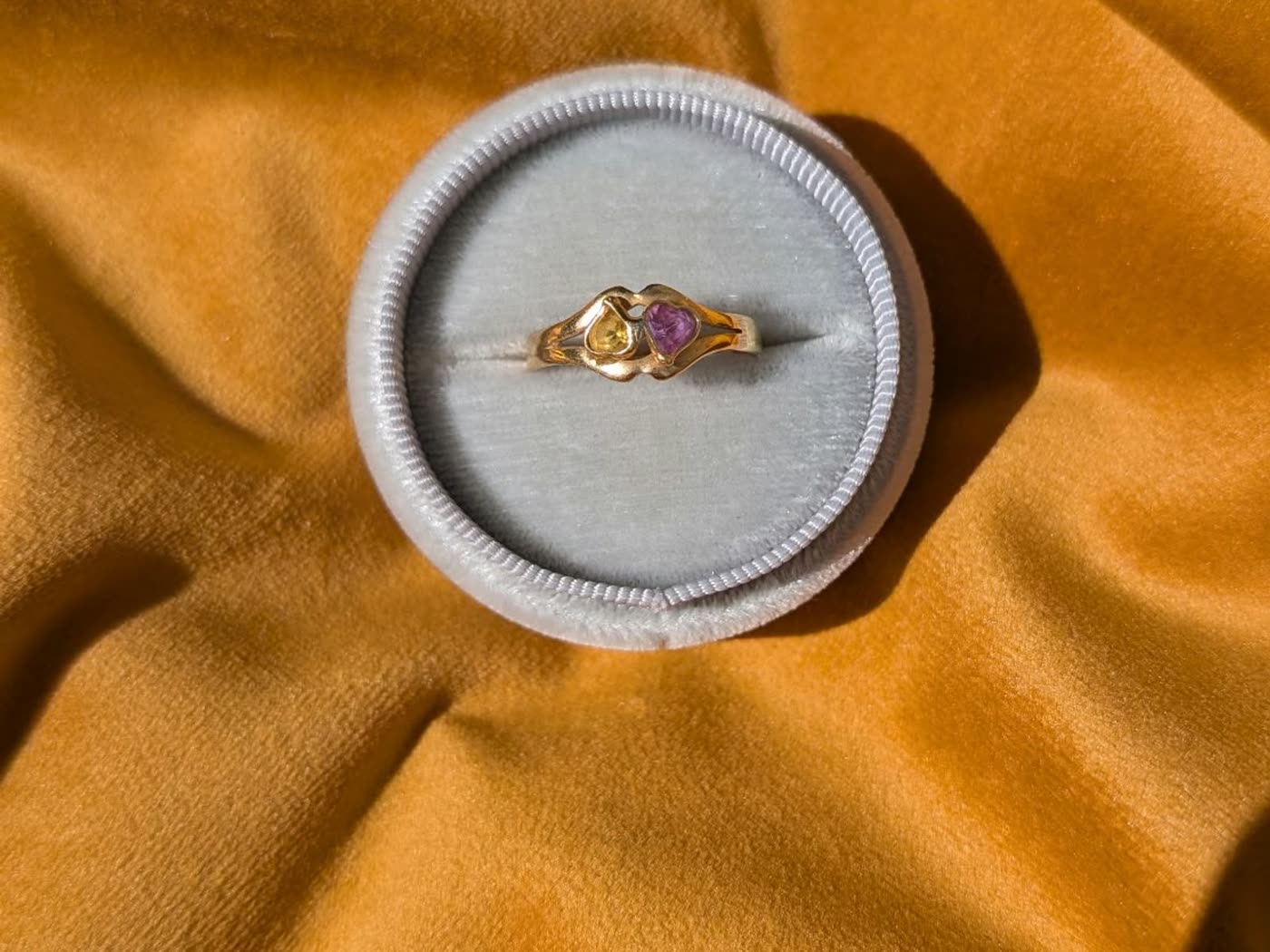 Ring with two heart-shaped stones in a ring box on mustard velvet